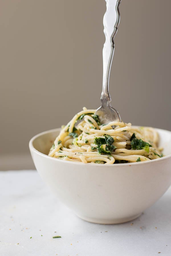 a bowl of creamy artichoke hummus spinach pasta with a fork sticking out of it.