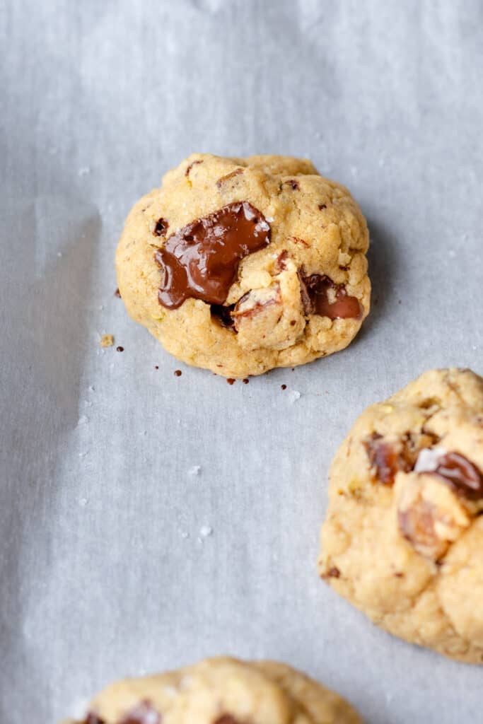 a few date pistachio chocolate chunk cookies on a parchment-lined baking sheet