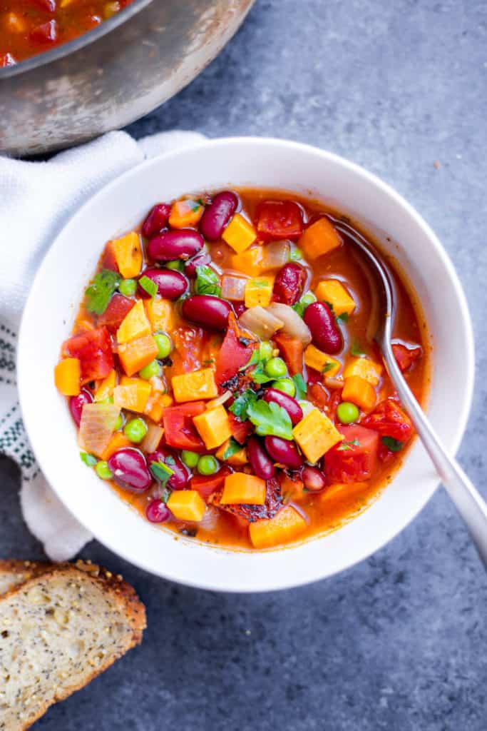 A bowl of vegetable soup with a spoon and a piece of bread