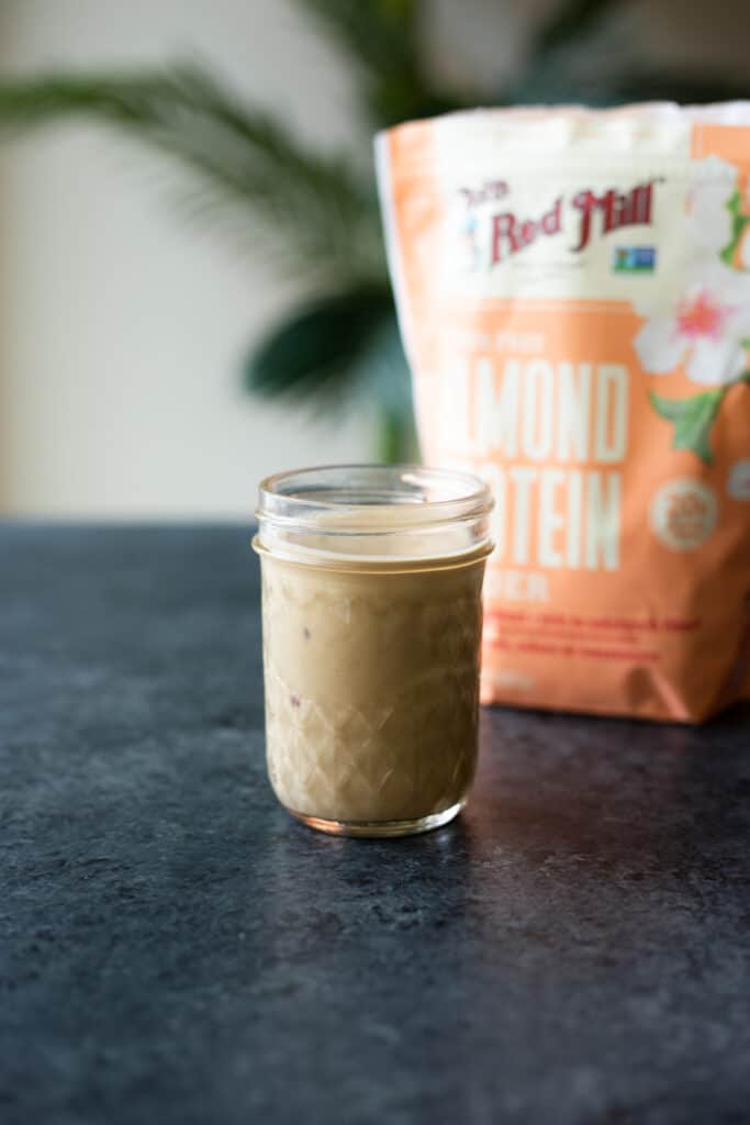 Garlicky Gingery Almondy Protein Sauce in a jar with a bag of Bob's Red Mill's Almond Protein Powder in the background