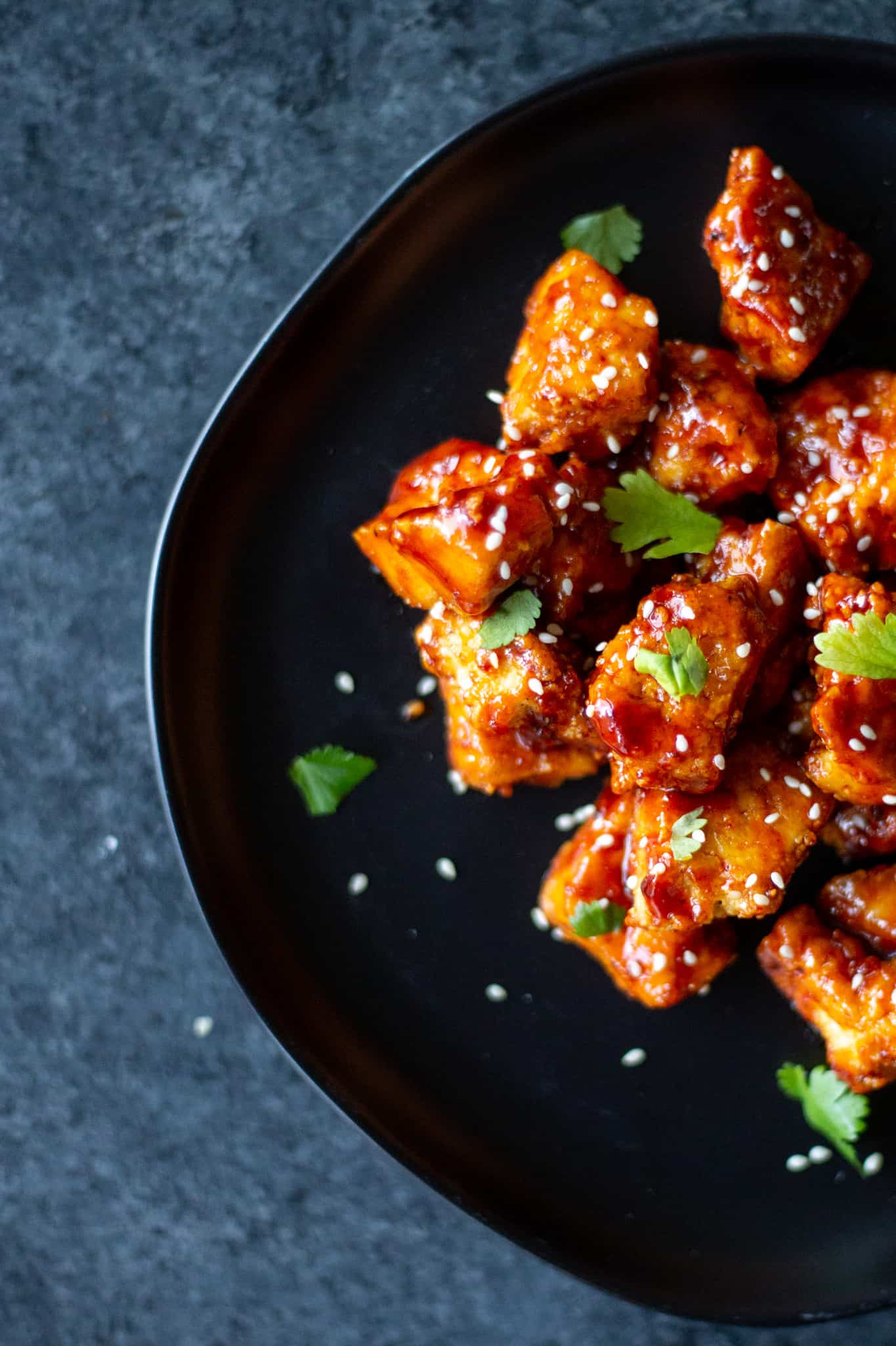 gochujang maple tofu nuggets on a black plate topped with cilantro and sesame seeds