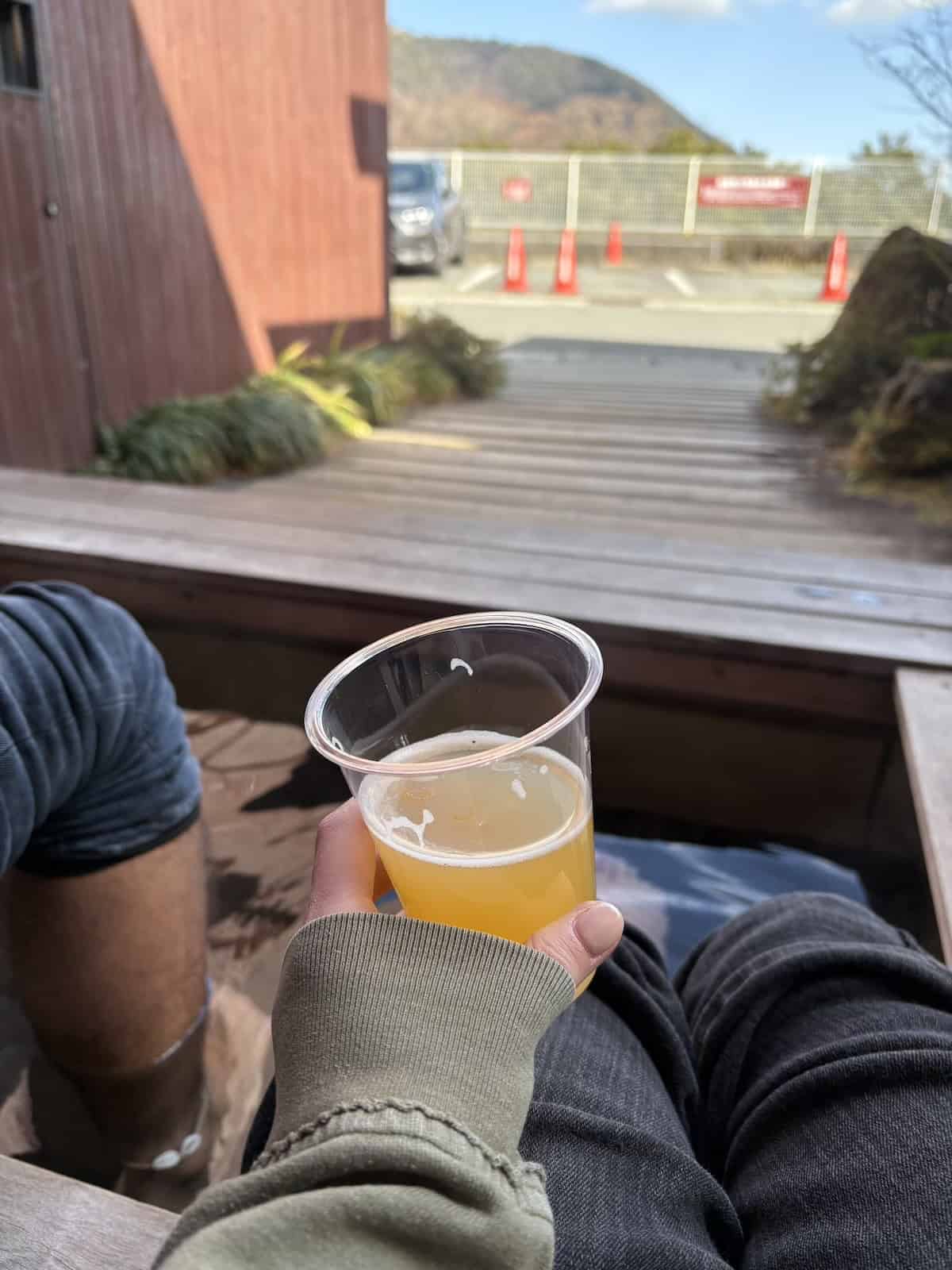 A hand holding a beer and the person's feet in a foot onsen