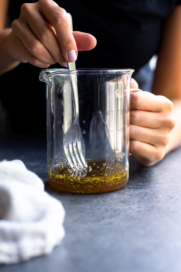 Hands whisking dressing with a fork in a measuring cup