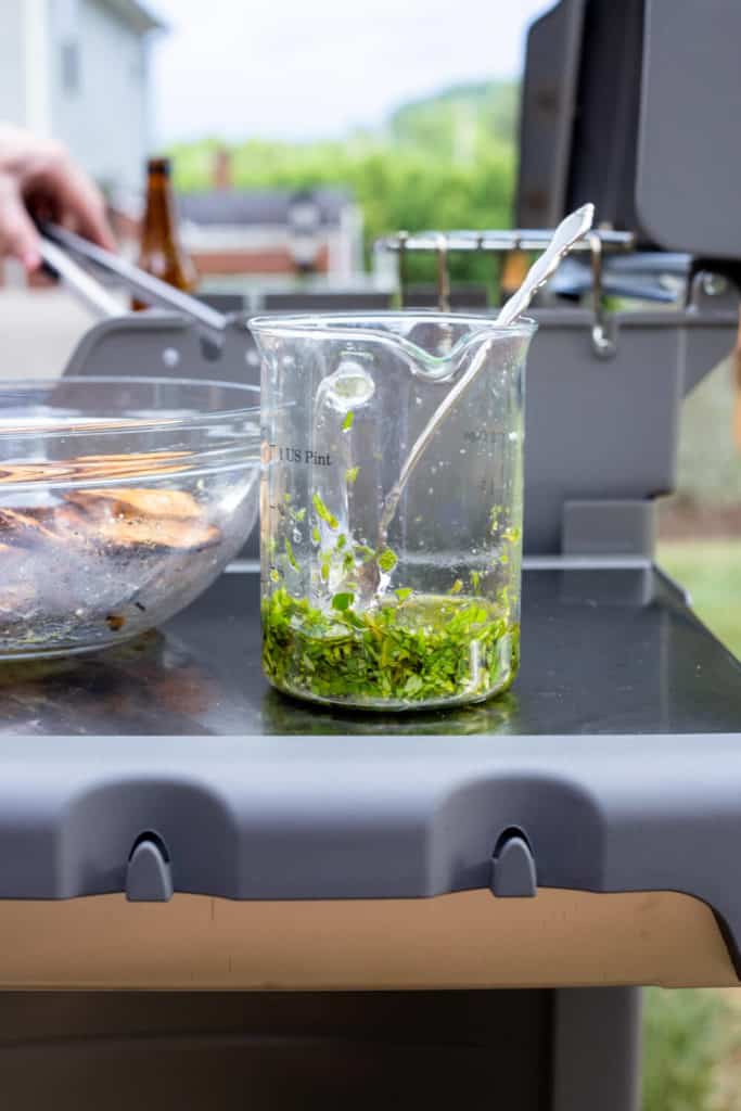 a jar of herb oil on the grill with a spoon sticking out of it