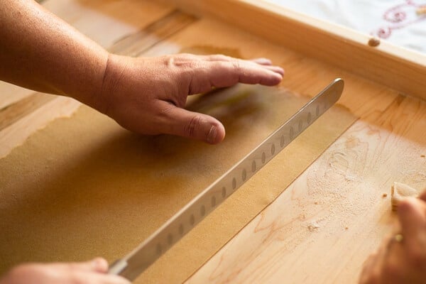 two hands cutting a sheet of pasta dough with a knife