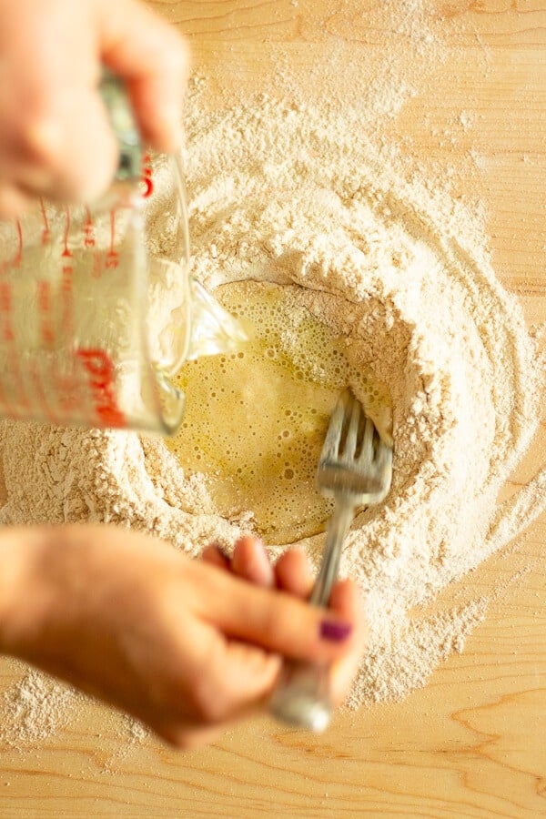 pouring liquid into a mound of flour with a fork mixing