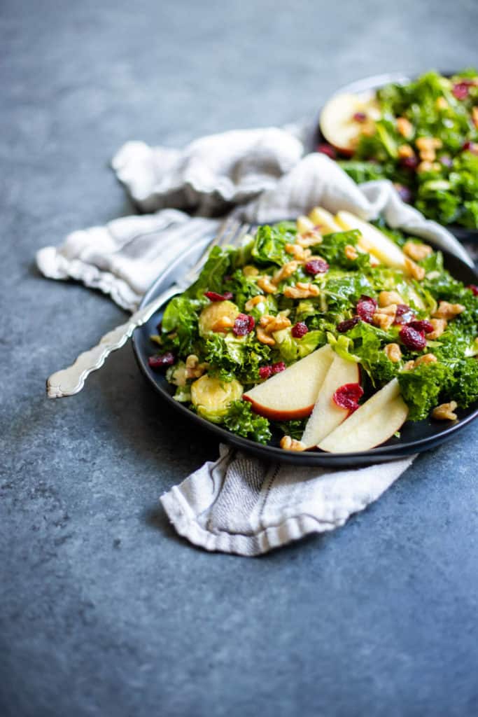 two plates of a Kale Brussels Sprout Salad with Maple Dijon Dressing on a dark background
