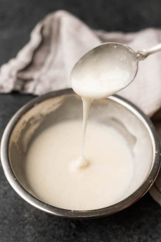 vanilla bean glaze dripping off of a spoon into a stainless steel bowl