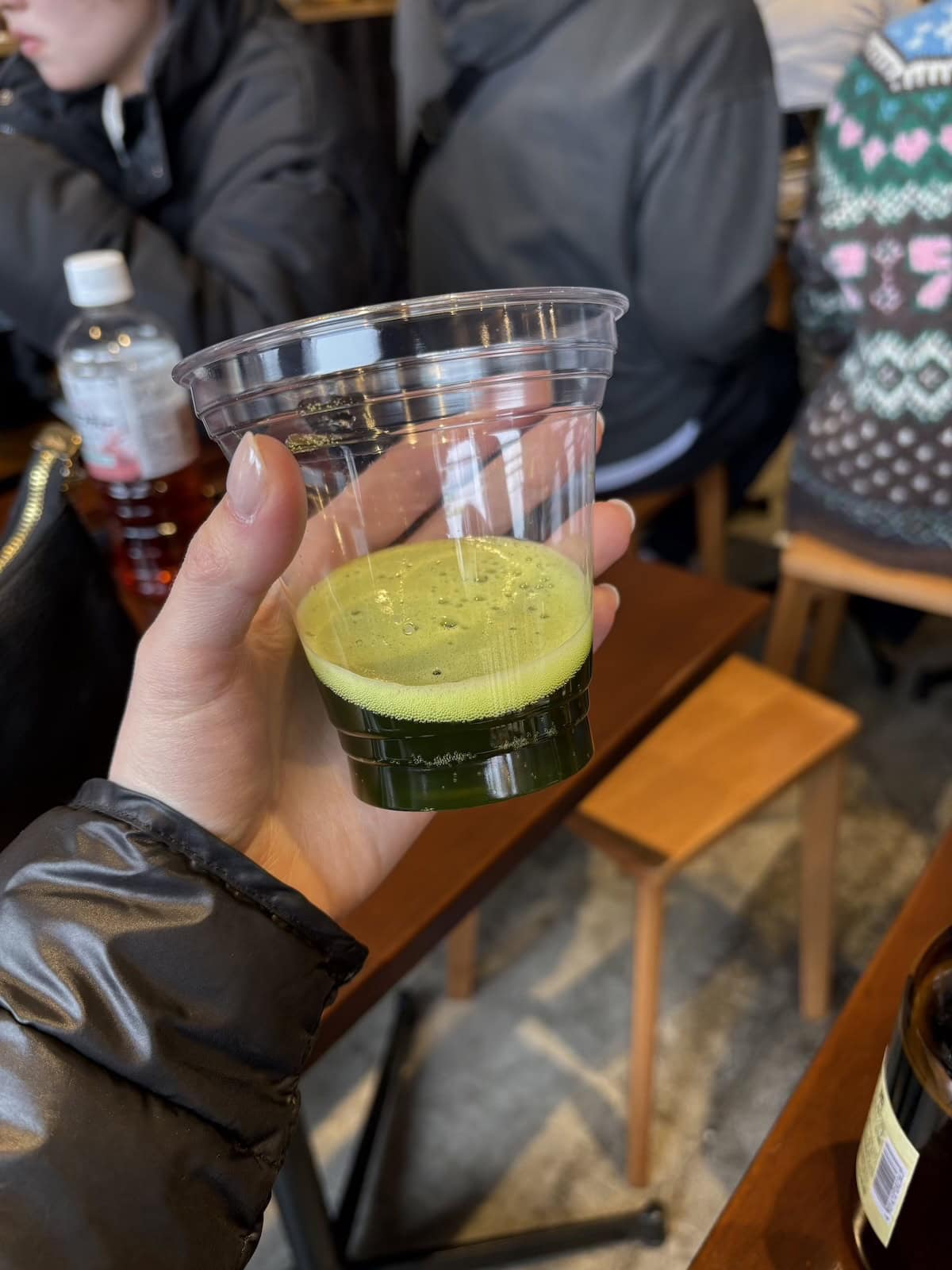 A hand holding a plastic cup with green matcha beer inside