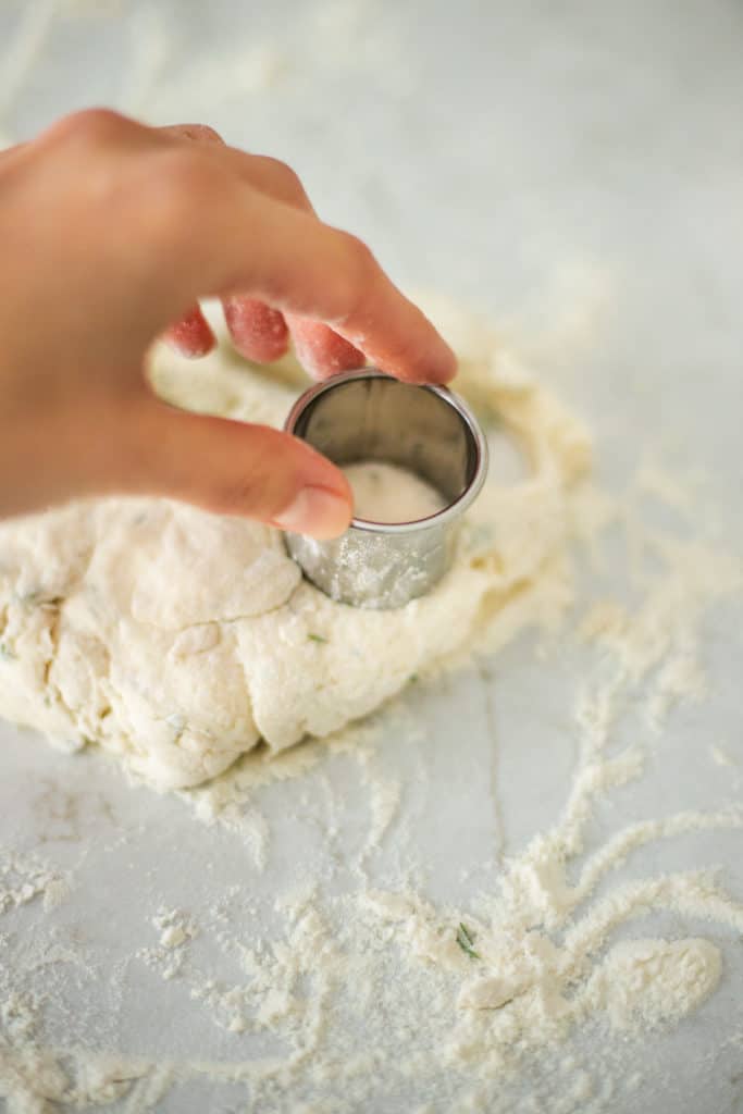 a hand punching out a mini vegan herb biscuitt
