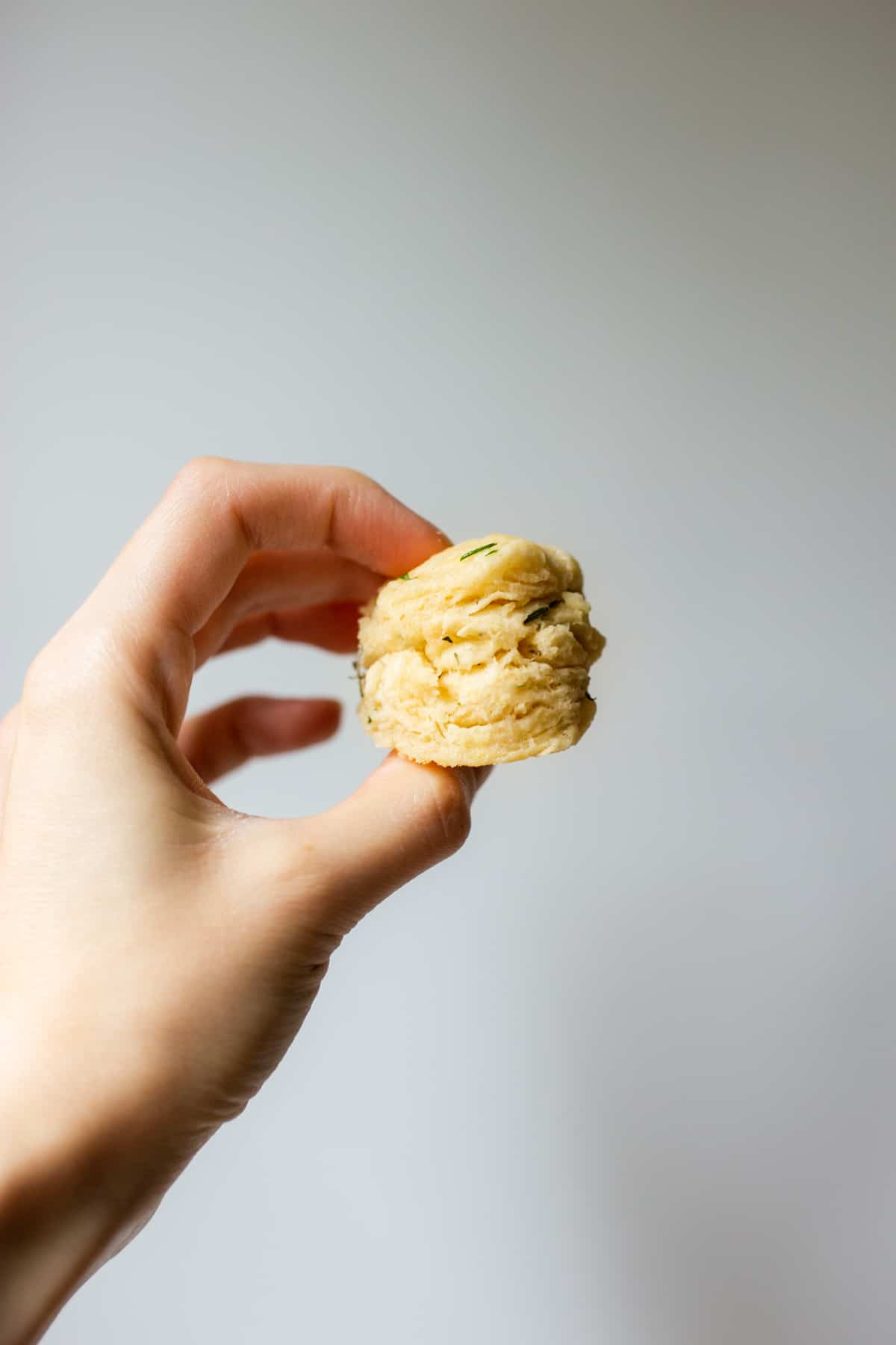 a hand holding up a mini vegan herb biscuit