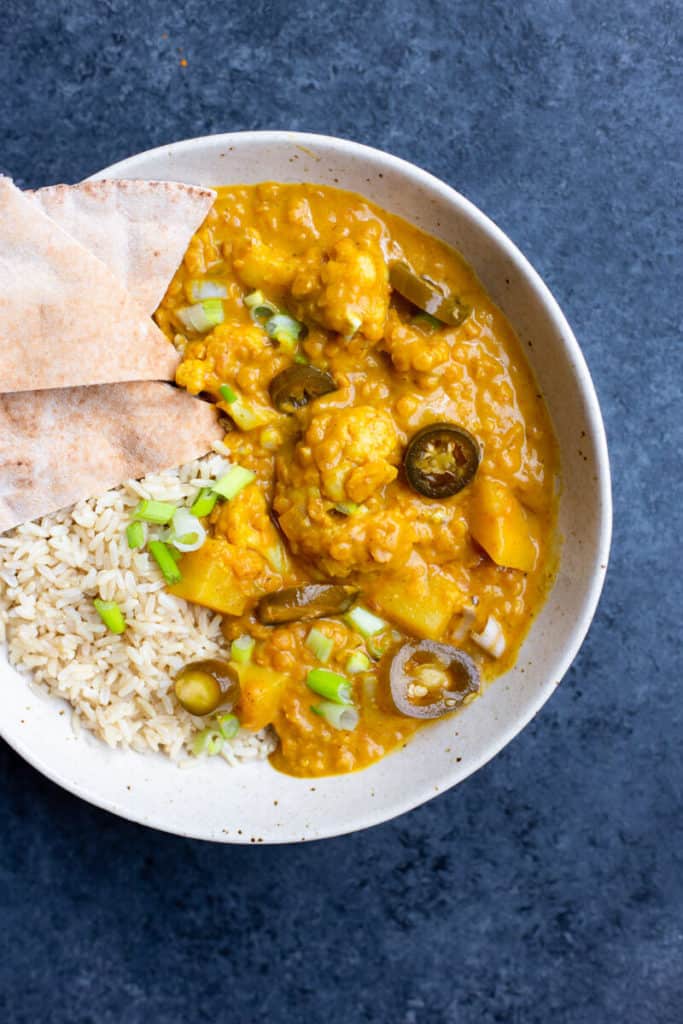 a bowl of One-Pot Potato Cauliflower Curry with rice, green onions, pita, and jalapeno on top