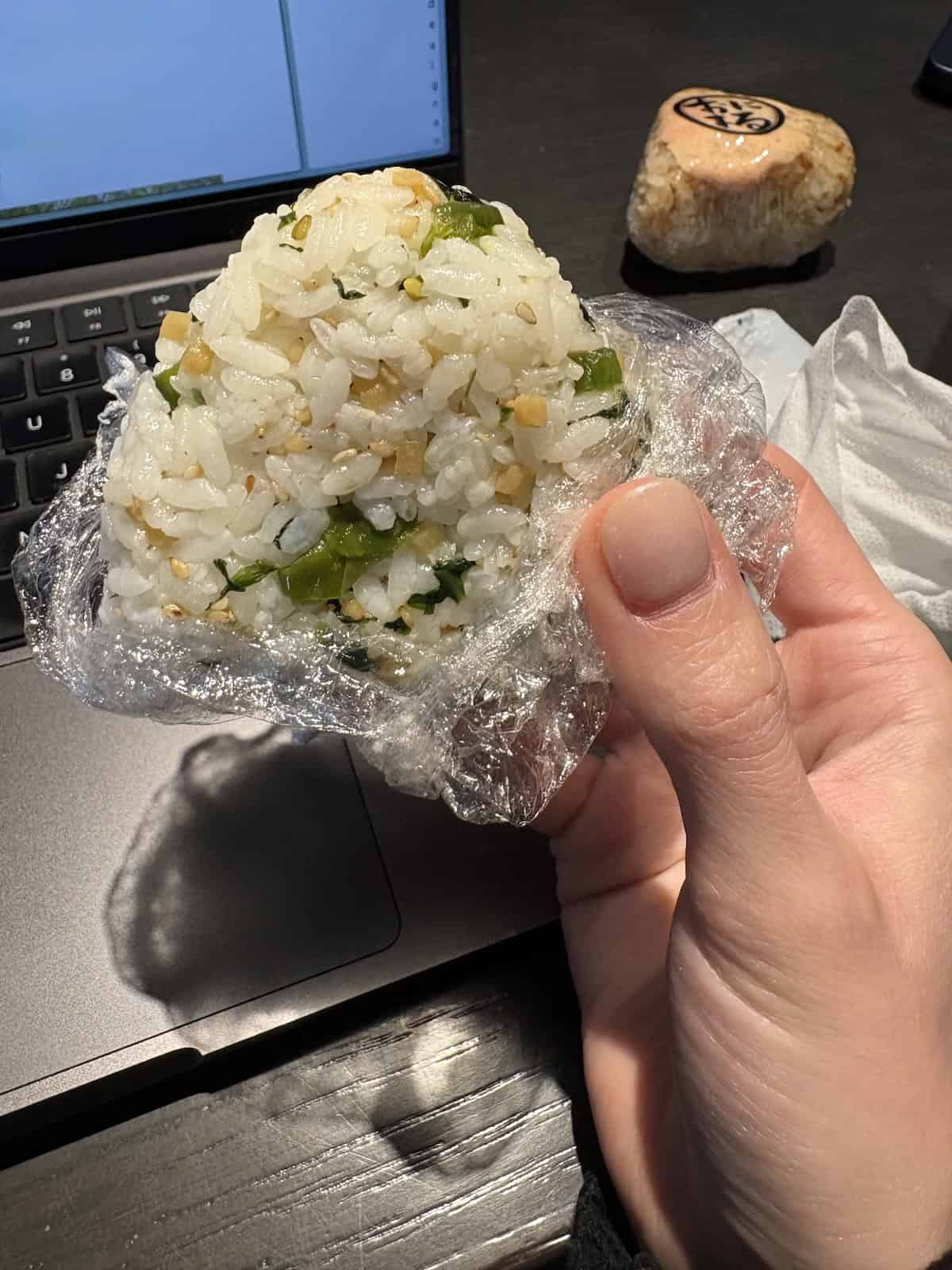 a hand holding a pickled mustard green and ginger onigiri