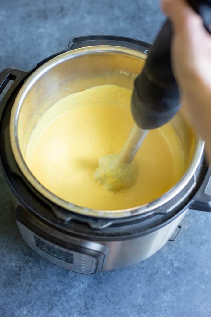 an immersion blender blending a creamy vegan cheese sauce in an Instant Pot