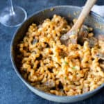 creamy roasted red pepper hummus pasta in a skillet with a wooden spoon sticking out of it
