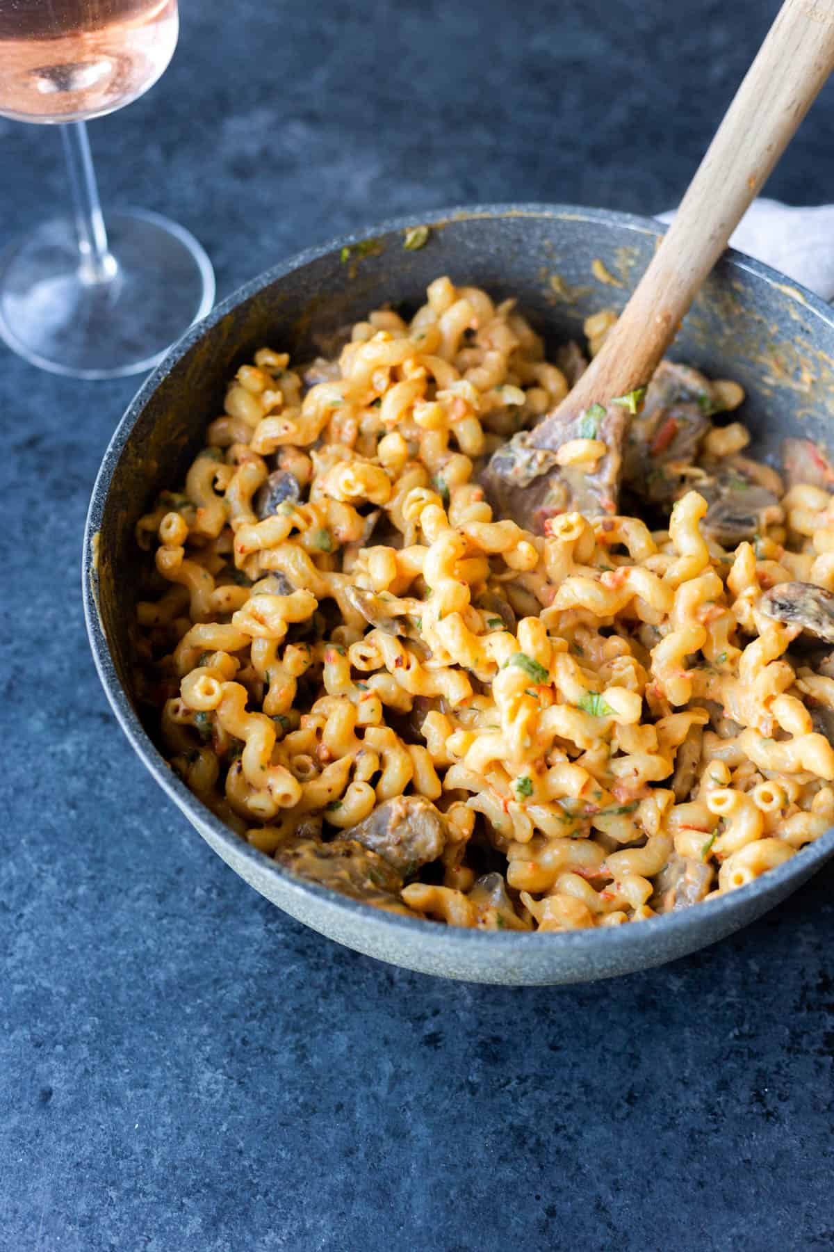 creamy roasted red pepper hummus pasta in a skillet with a wooden spoon sticking out of it