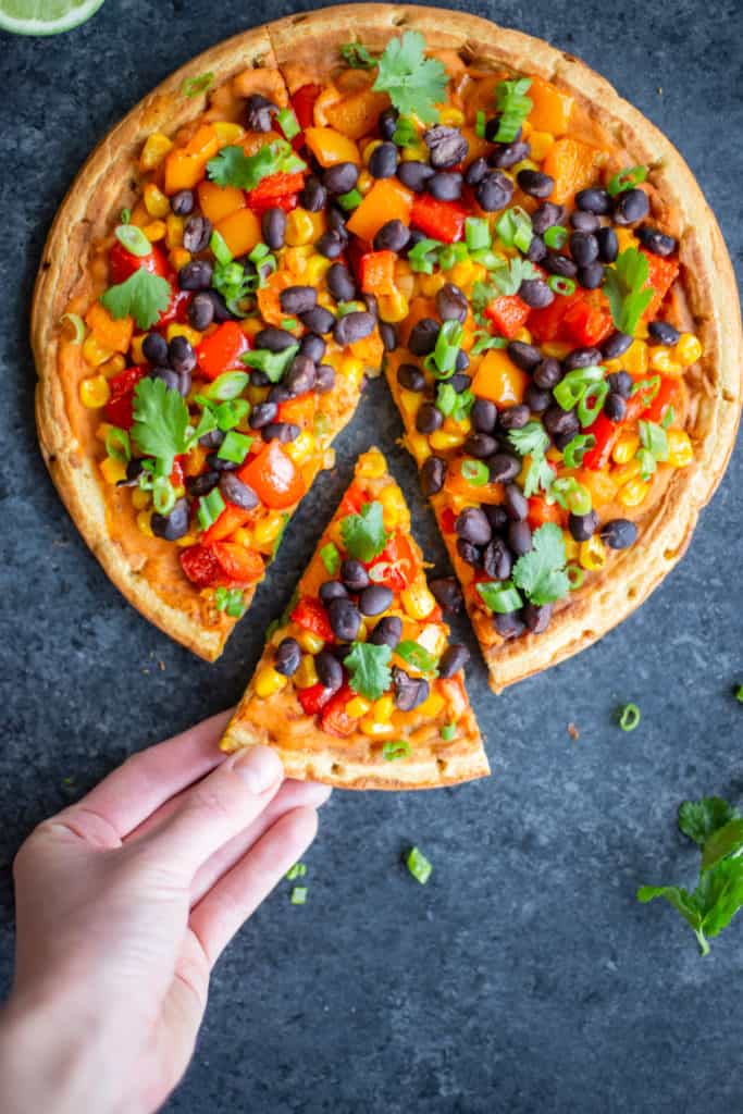 a hand taking a slice of the Smoky Pepper, Corn, and Black Bean Flatbread