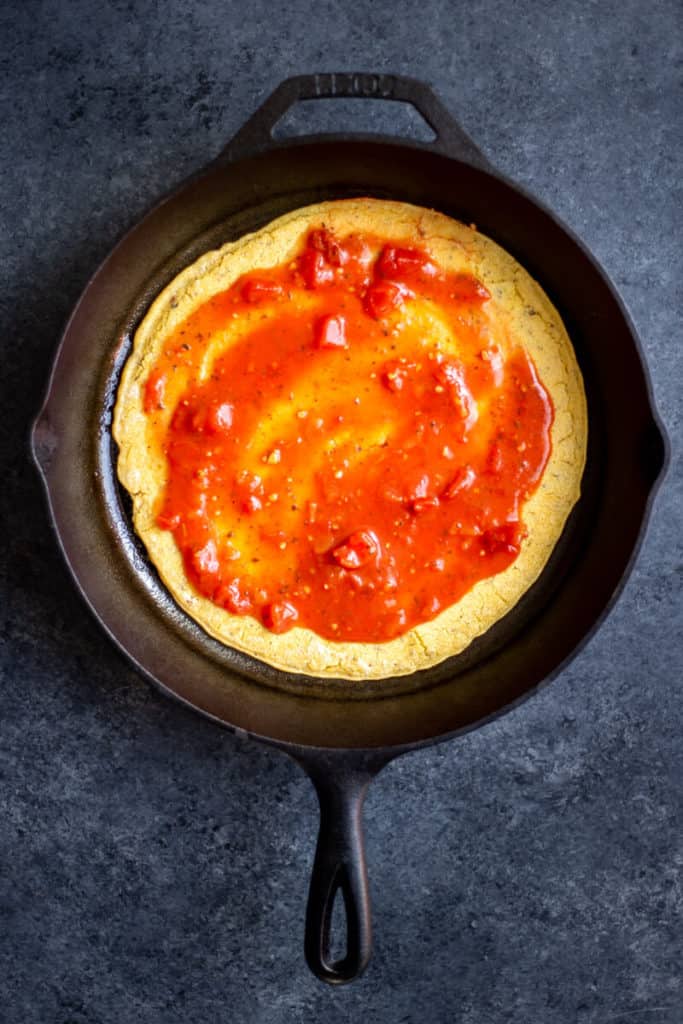 cooked socca flatbread in a cast iron skillet with marinara sauce on top
