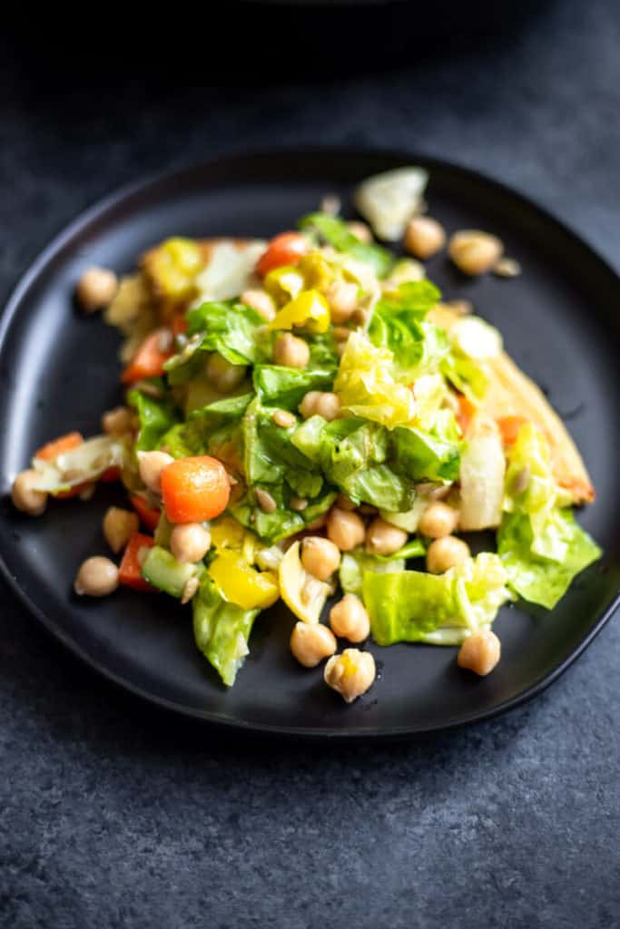 A slice of socca salad pizza on a black plate