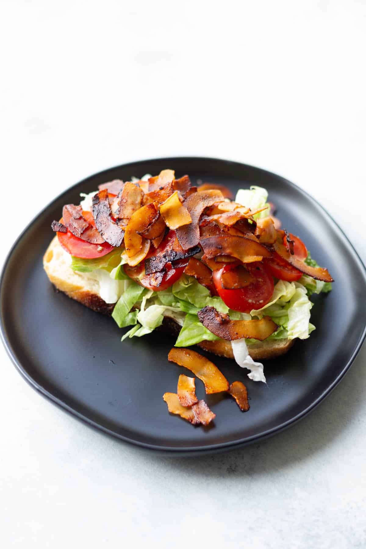 a topless vegan blt made with coconut bacon on a black plate