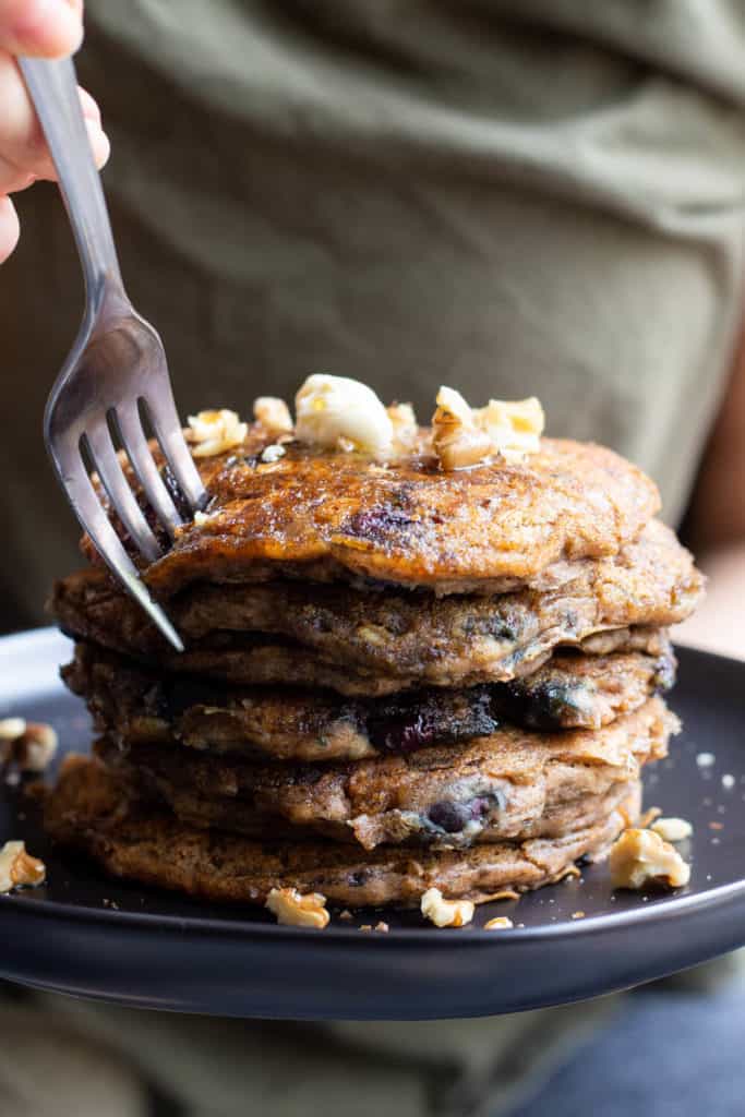 a hand sticking a fork into a stack of pancakes