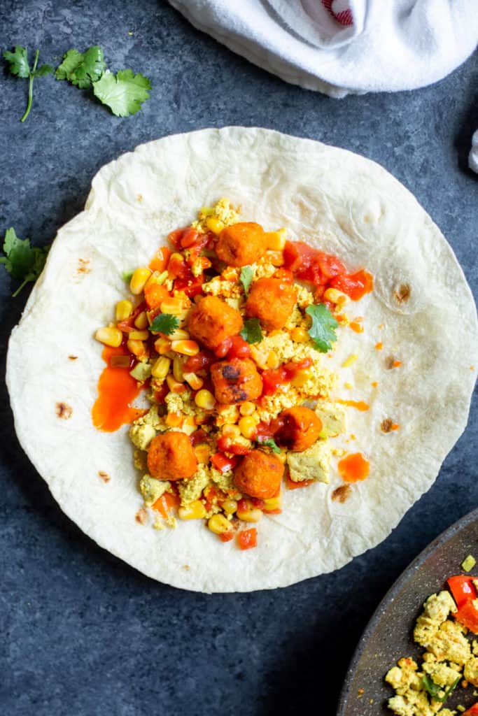 tofu scramble, salsa, hot sauce, avocado, and tater tots on a tortilla