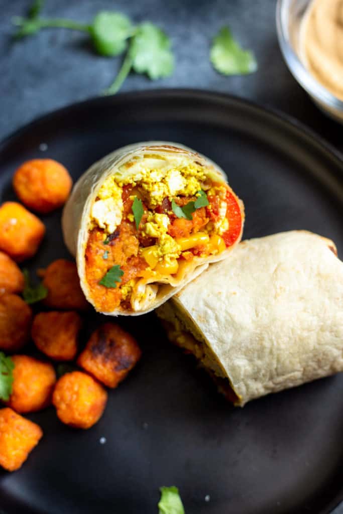 a sliced vegan breakfast burrito on a black plate