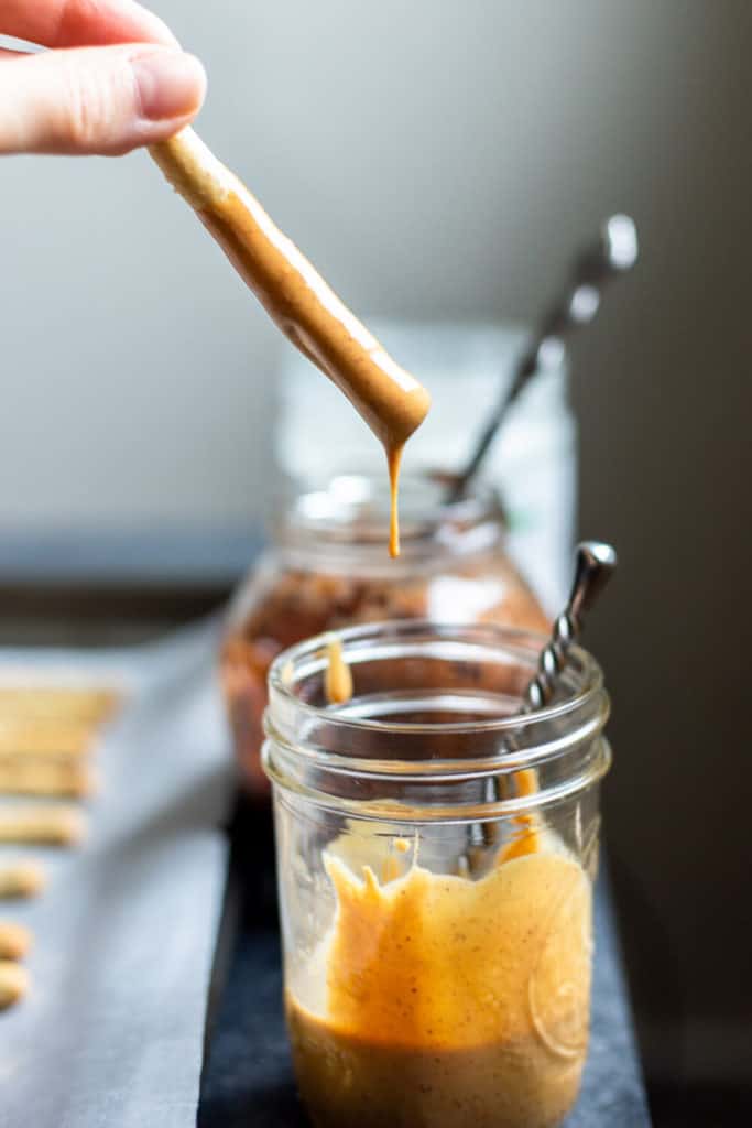 a pretzel sticks being pulled out of a jar of melted peanut butter
