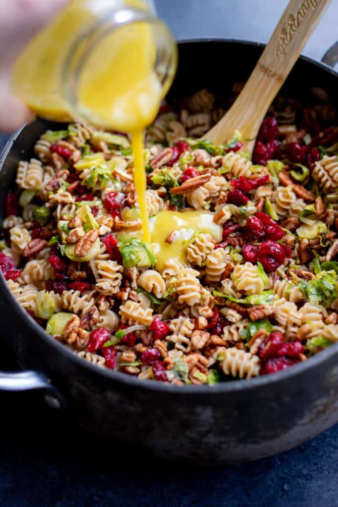 Hand pouring dressing into a pot of Vegan Fall Pasta Salad
