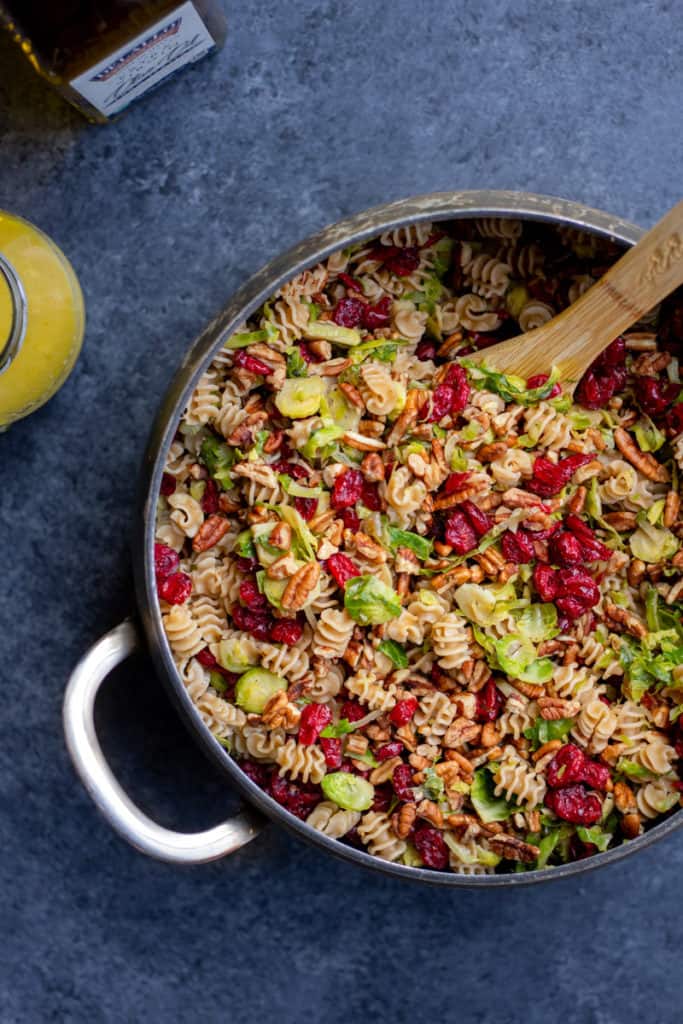 Vegan Fall Pasta Salad in a pot with a wooden spoon and dressing off to the side