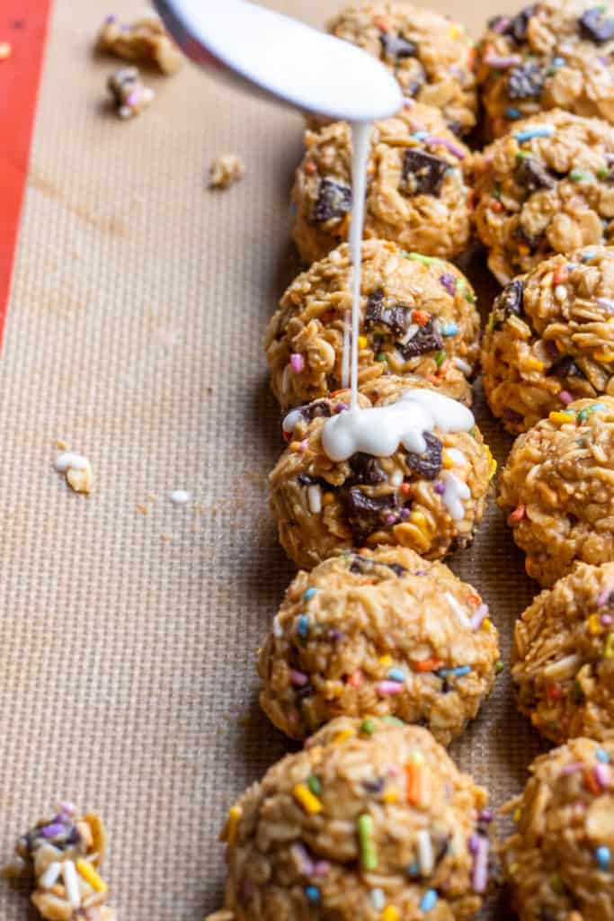 a spoon pouring icing over funfetti no-bake cookies