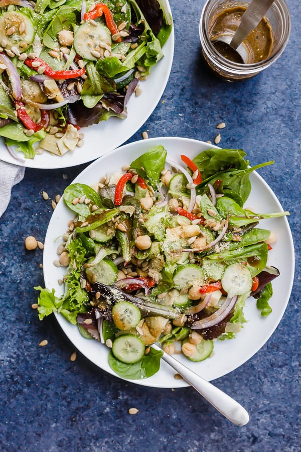 two italian chopped salads on plates with a jar of dressing