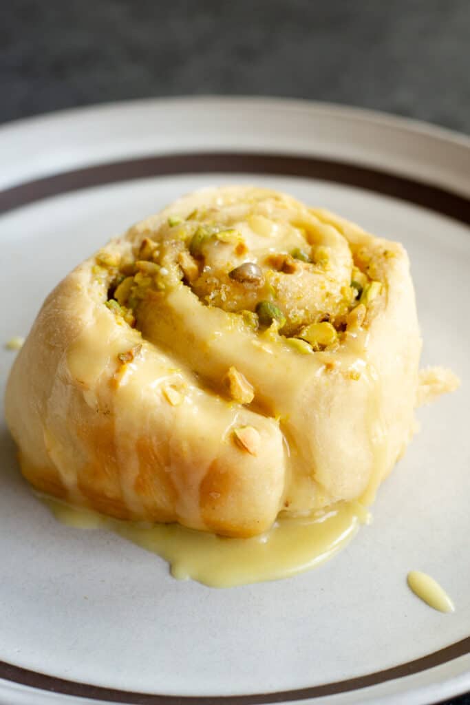 a vegan lemon pistachio sweet roll on a plate topped with a lemon glaze